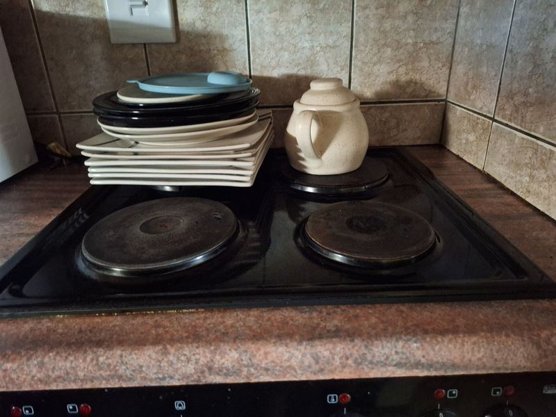 Close-up view of a dated electric hob with tiled backsplash and laminate countertop in a kitchen setting.