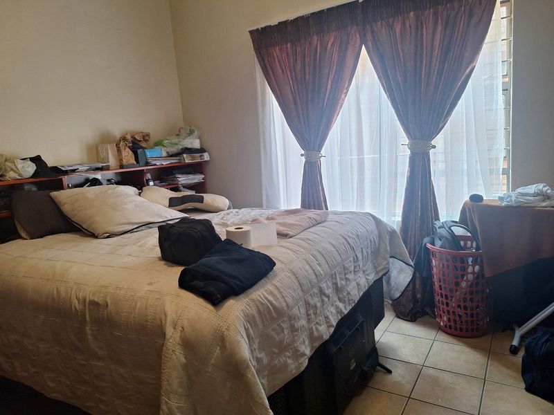 A bedroom featuring tiled flooring and a window fitted with security bars, providing natural light.