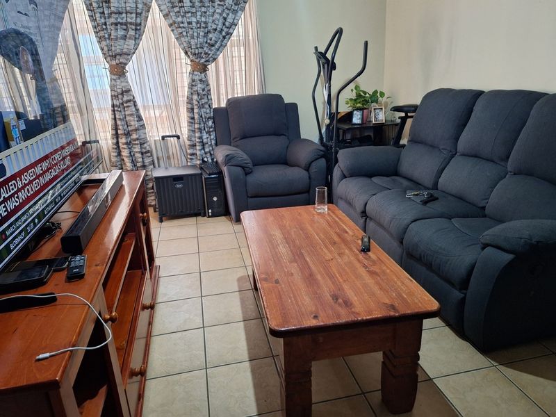 A living room area featuring tiled flooring and large windows with curtains, providing a functional space for relaxation.