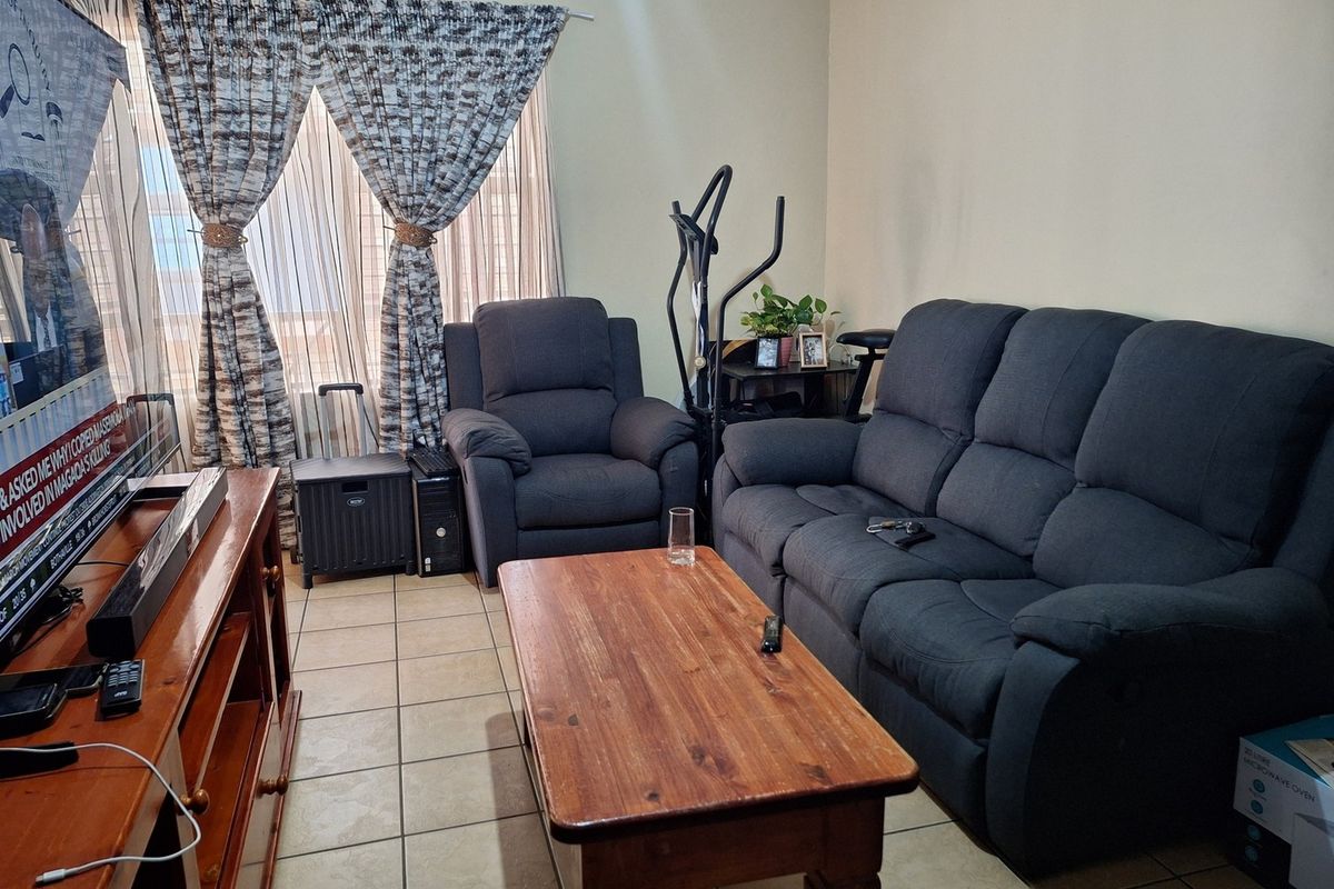A functional living room featuring ceramic floor tiles and large windows with curtain tracks, providing a neutral base for potential interior updates.