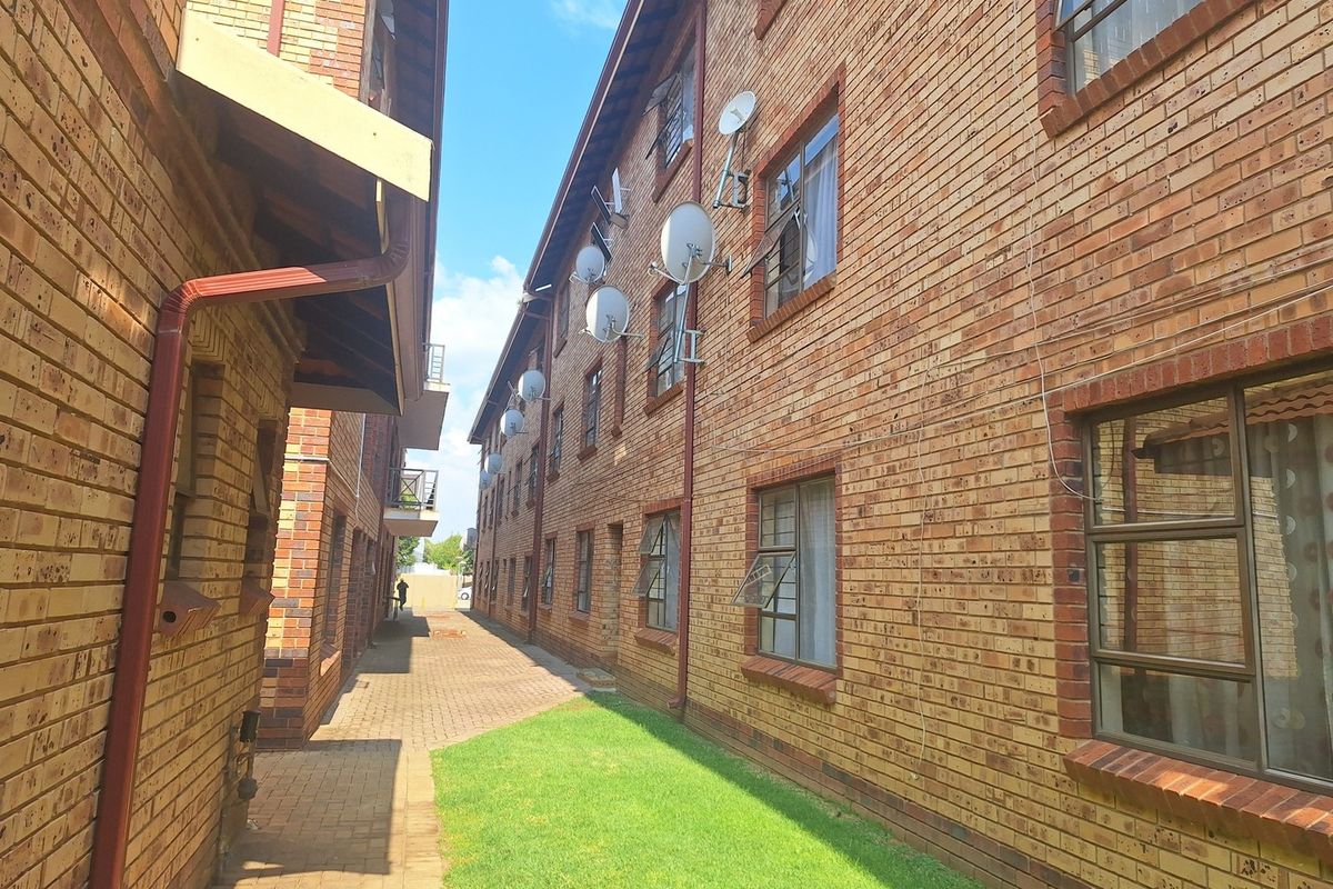 Exterior view of the apartment complex featuring face brick walls, paved walkways, and a small lawn area between the building blocks.