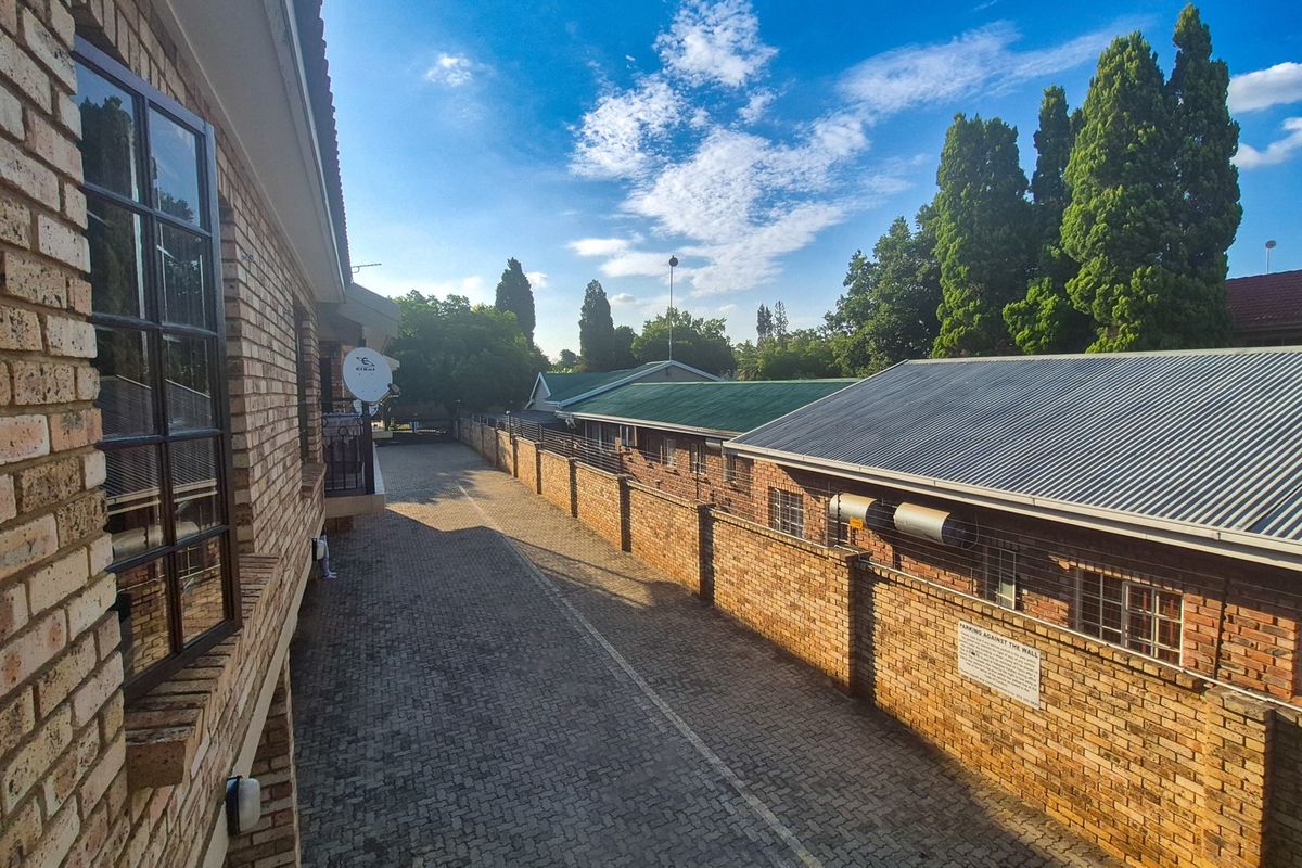 An elevated view of the rear exterior area featuring face brick buildings, a paved driveway, and a secure boundary wall.