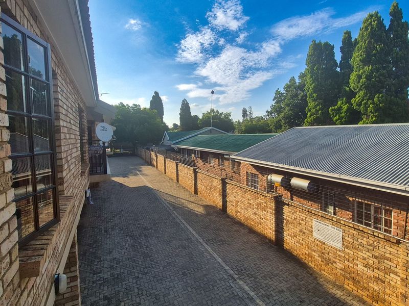 An elevated view of the rear exterior area featuring face brick buildings, a paved driveway, and a secure boundary wall.