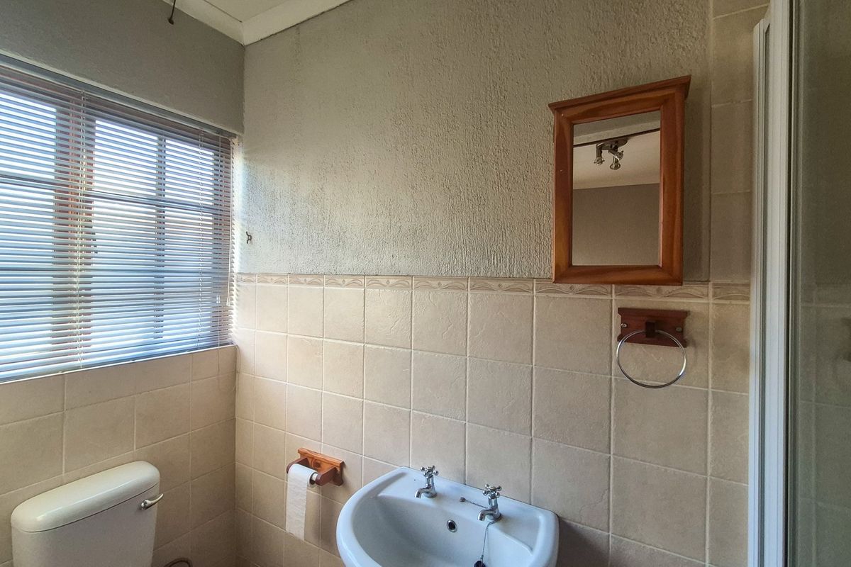 A functional bathroom featuring a pedestal basin, toilet, and shower enclosure with neutral wall tiling and a wall-mounted mirror cabinet.