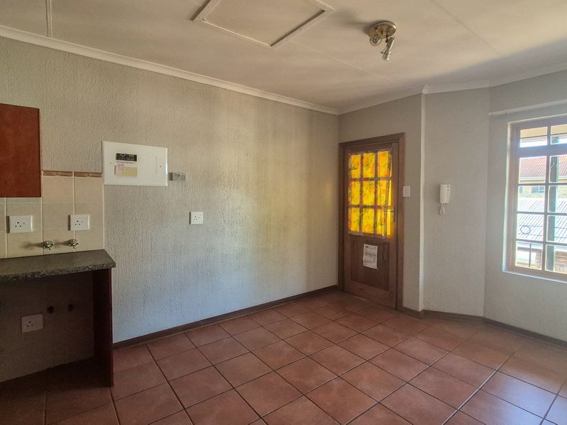 An empty kitchen area featuring tiled flooring, built-in cabinetry with laminate countertops, and a timber framed exterior door.