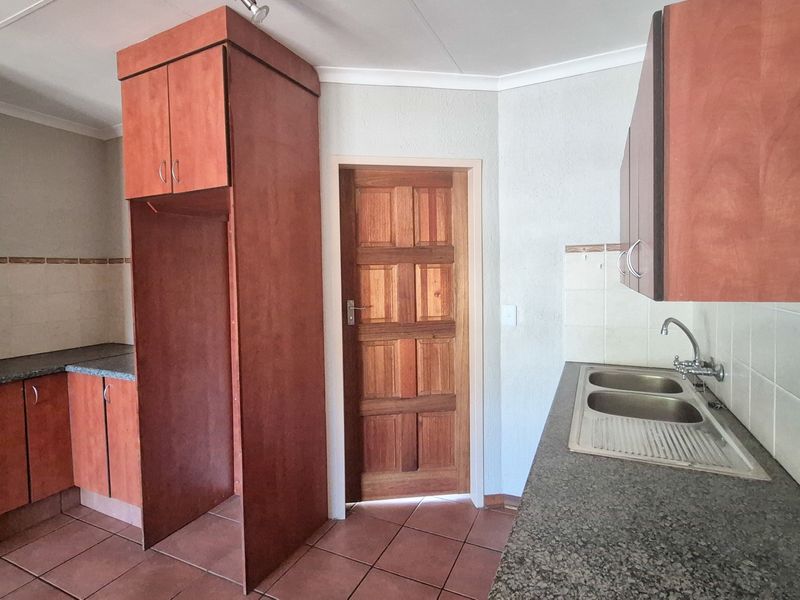 A functional kitchen featuring built-in wooden cabinetry, laminate countertops, a double stainless steel sink, and tiled flooring.