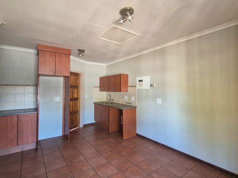 A functional, empty kitchen area featuring built-in wooden cabinetry, laminate countertops, a stainless steel sink, and tiled flooring throughout.