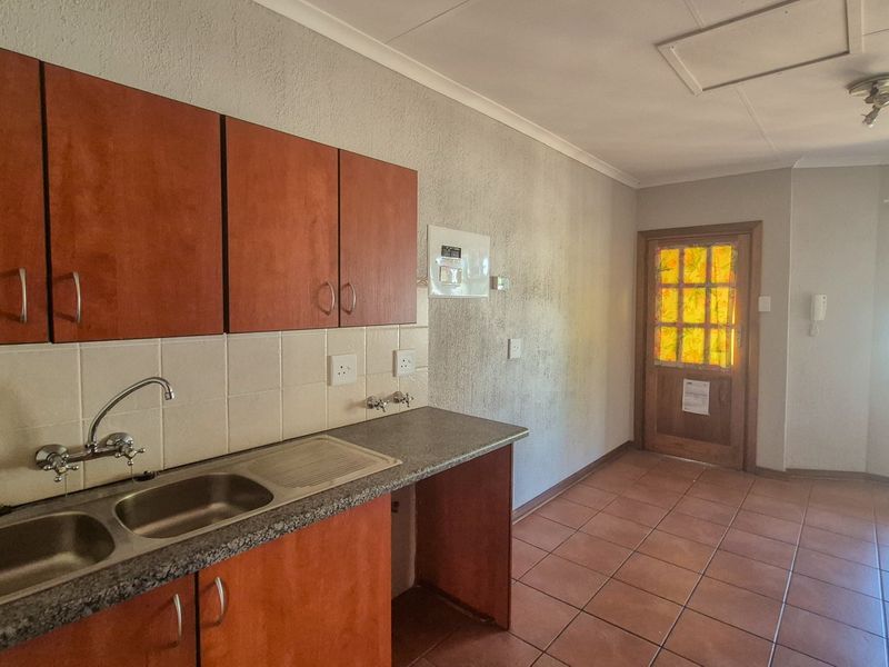 A functional kitchen area featuring built-in cabinetry, a double sink, tiled flooring, and direct access to an exterior door.