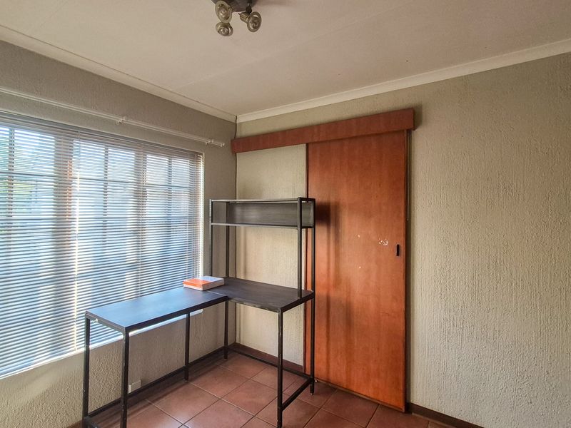 A bedroom featuring tiled flooring, a sliding door, and venetian blinds, offering a functional space with potential for cosmetic updates.