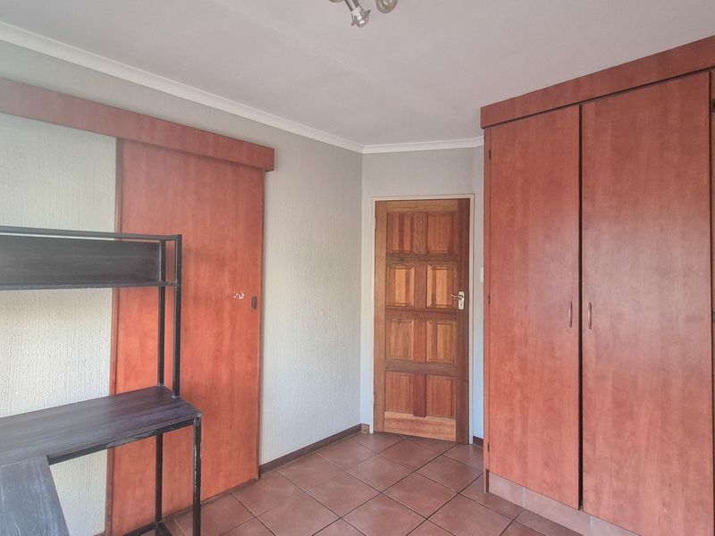 Bedroom featuring tiled flooring, built-in wooden cupboards, and a traditional wooden door, offering a functional space with potential for cosmetic updates.