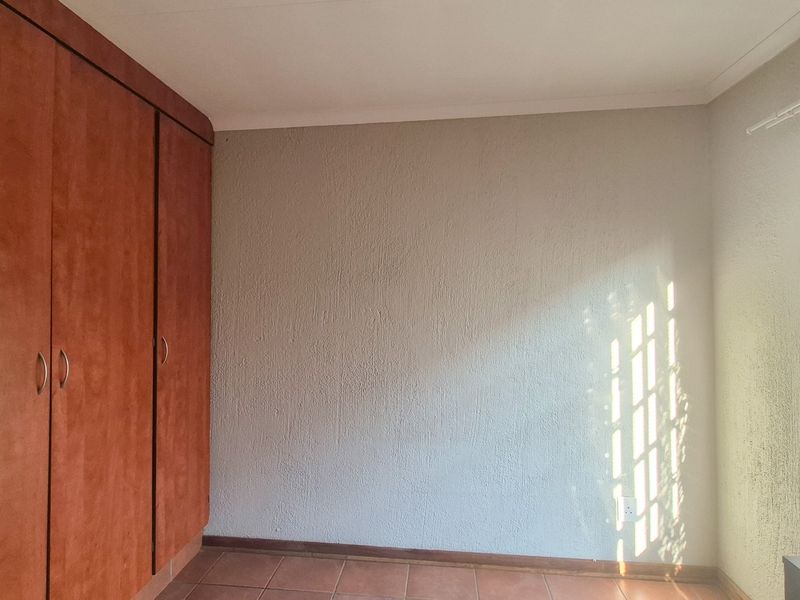 A bright, empty bedroom featuring built-in wooden cupboards, tiled flooring, and venetian blinds, offering a clean canvas for personalization.
