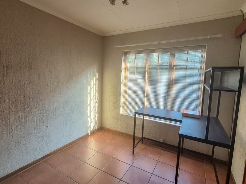 A bright, empty bedroom featuring tiled flooring, a built-in cupboard, and venetian blinds, offering a clean and versatile space.