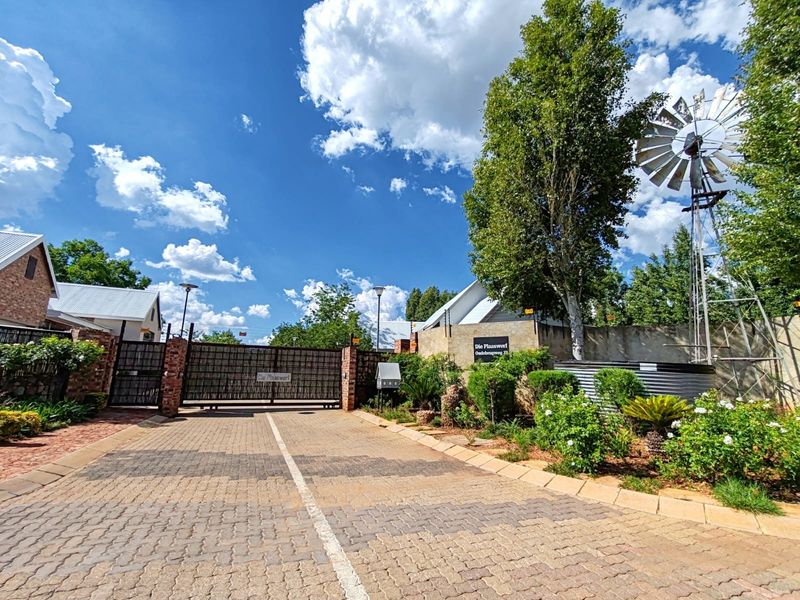 Front entrance view of the property featuring a paved driveway, secure gated access, brick boundary walls, and a decorative windmill.