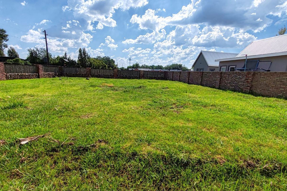 A spacious, level residential plot featuring a well-maintained grass lawn enclosed by a secure brick perimeter wall and reed fencing.