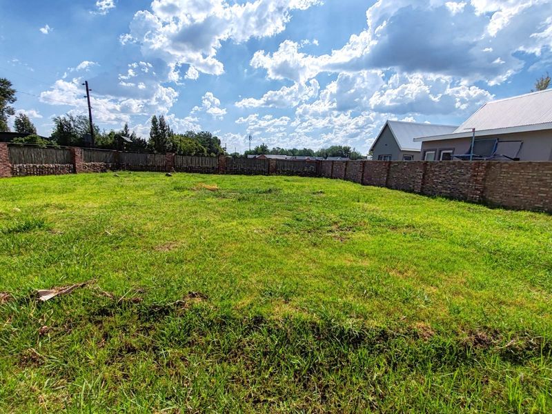 A spacious, level residential plot featuring a well-maintained grass lawn enclosed by a secure brick perimeter wall and reed fencing.