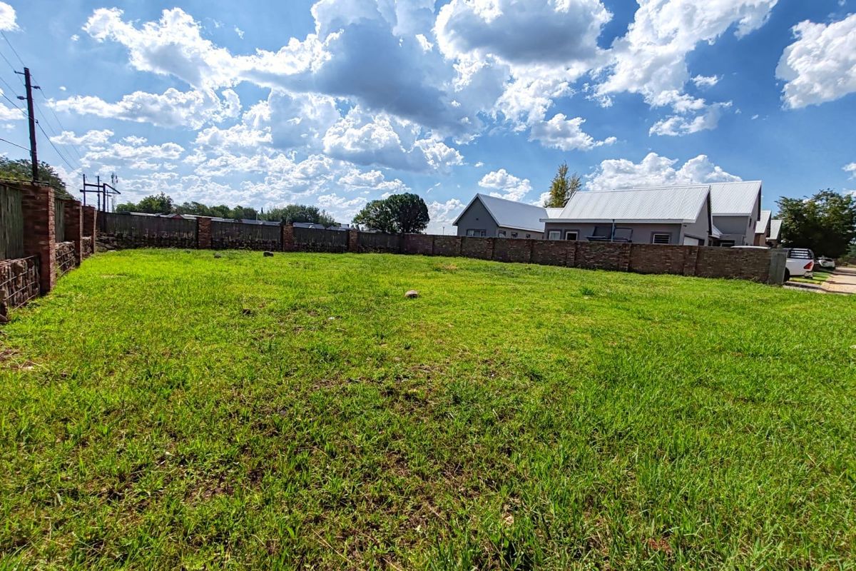 A vacant residential plot featuring a well-maintained grass lawn enclosed by a sturdy brick boundary wall.