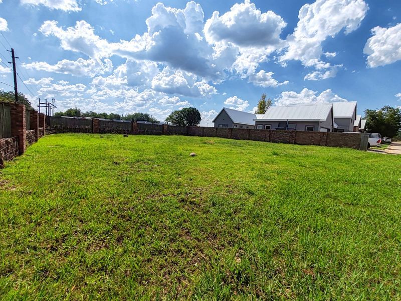 A vacant residential plot featuring a well-maintained grass lawn enclosed by a sturdy brick boundary wall.