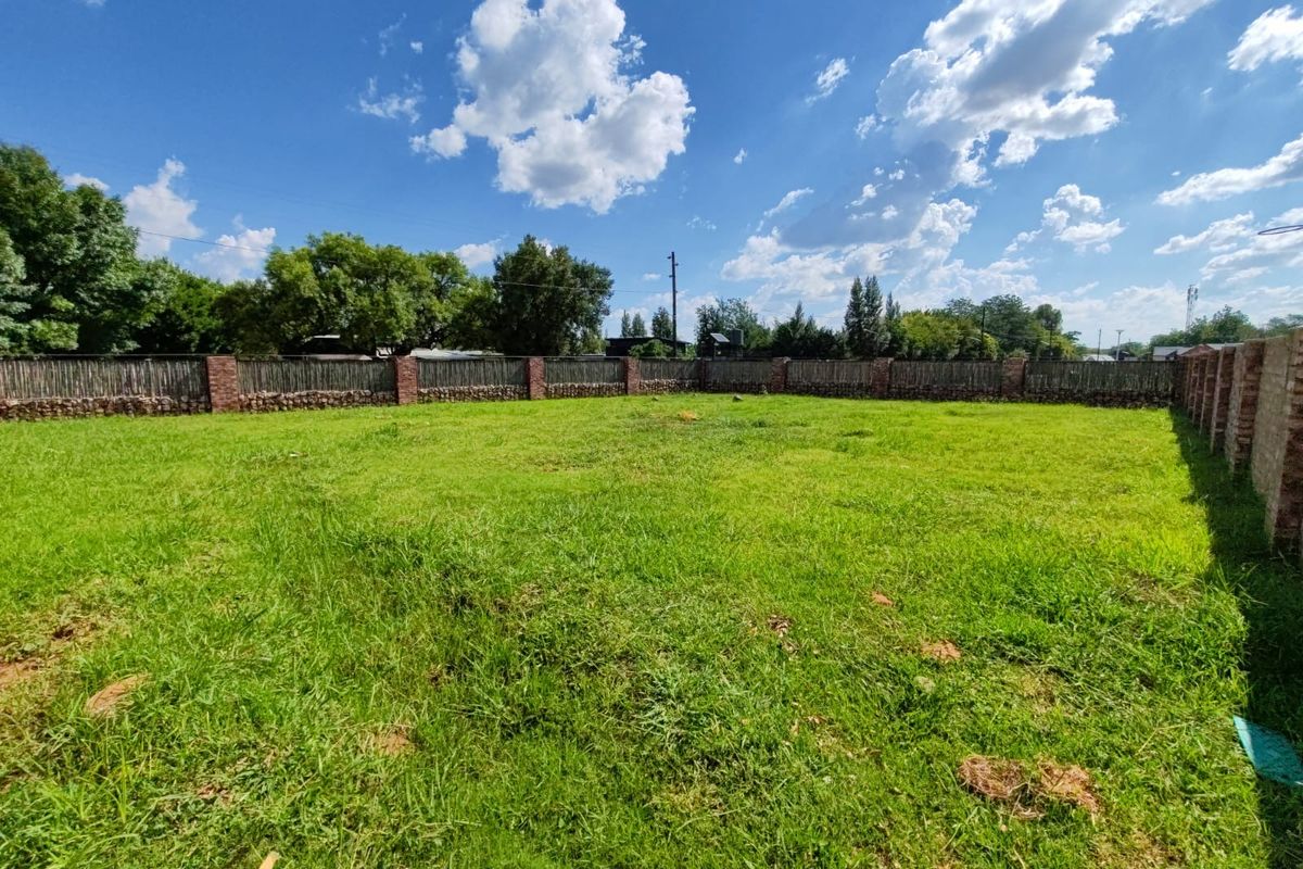 A spacious, level residential plot featuring a well-maintained grass lawn enclosed by a secure brick and timber perimeter fence.
