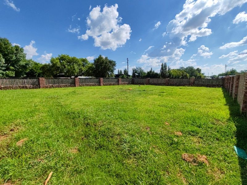 A spacious, level residential plot featuring a well-maintained grass lawn enclosed by a secure brick and timber perimeter fence.