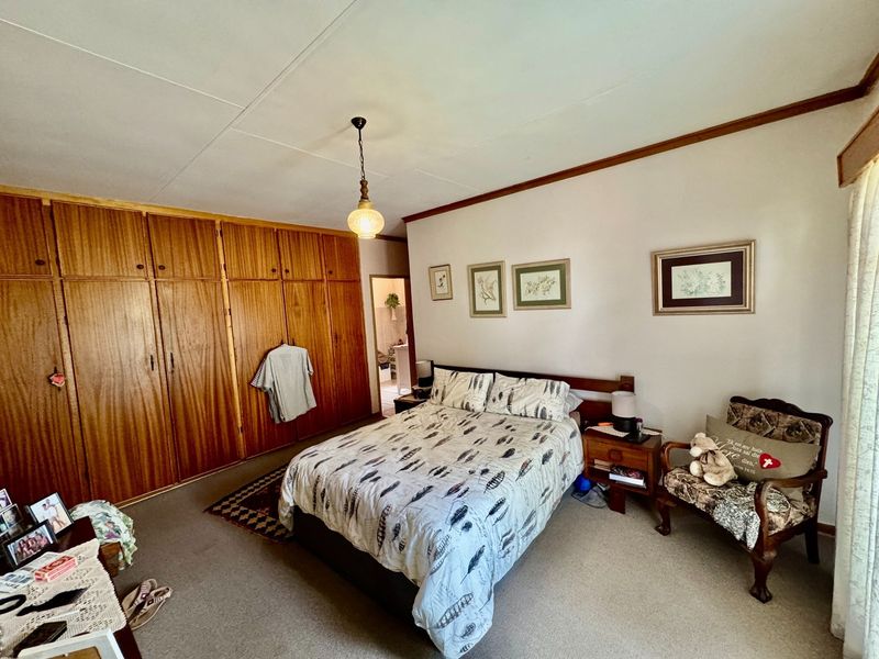 A spacious bedroom featuring extensive built-in wooden cabinetry, neutral walls, and carpeted flooring, offering a functional layout with potential for modern updates.