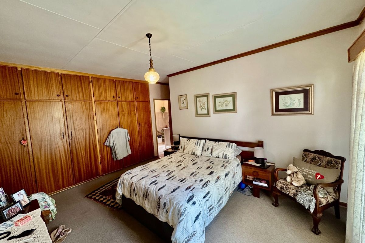 A spacious bedroom featuring extensive built-in wooden cabinetry, neutral walls, and carpeted flooring, offering a functional layout with potential for modern updates.