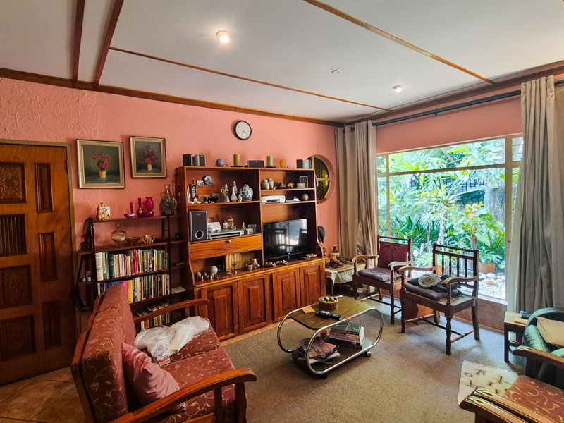 A comfortable living room featuring a large picture window with garden views, timber-panelled ceiling, and recessed lighting, offering a warm and inviting atmosphere.