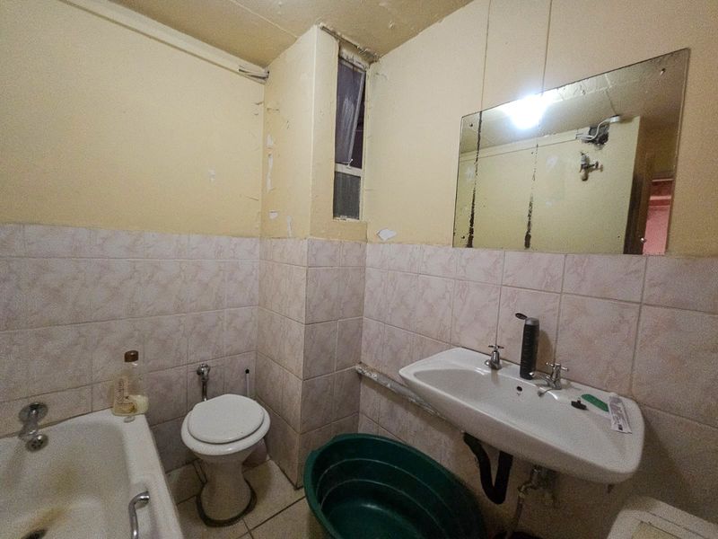 A dated bathroom featuring a bathtub, toilet, and pedestal sink, requiring significant cosmetic updates and repairs to the wall finishes and fixtures.