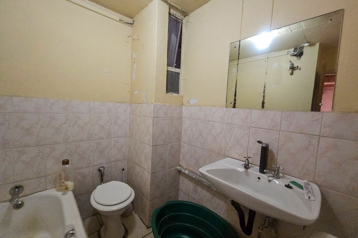 A dated bathroom featuring a bathtub, toilet, and pedestal sink, requiring significant cosmetic updates and repairs to the wall finishes and fixtures.
