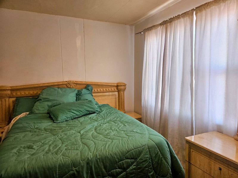 A bedroom featuring wall paneling and window treatments, requiring cosmetic updates to improve the overall aesthetic and finish quality.