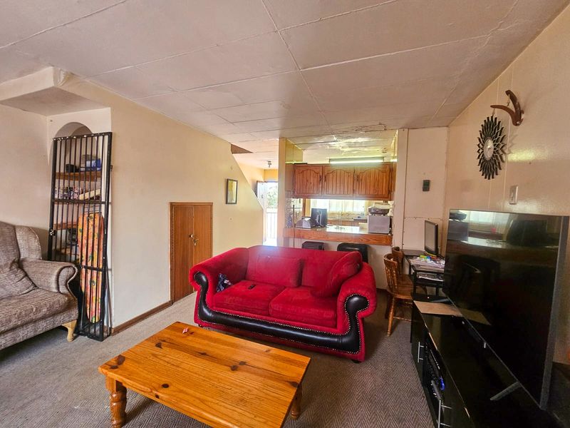 Open-plan living area featuring a connected kitchen with wooden cabinetry and a breakfast counter, showing signs of wear and ceiling damage.