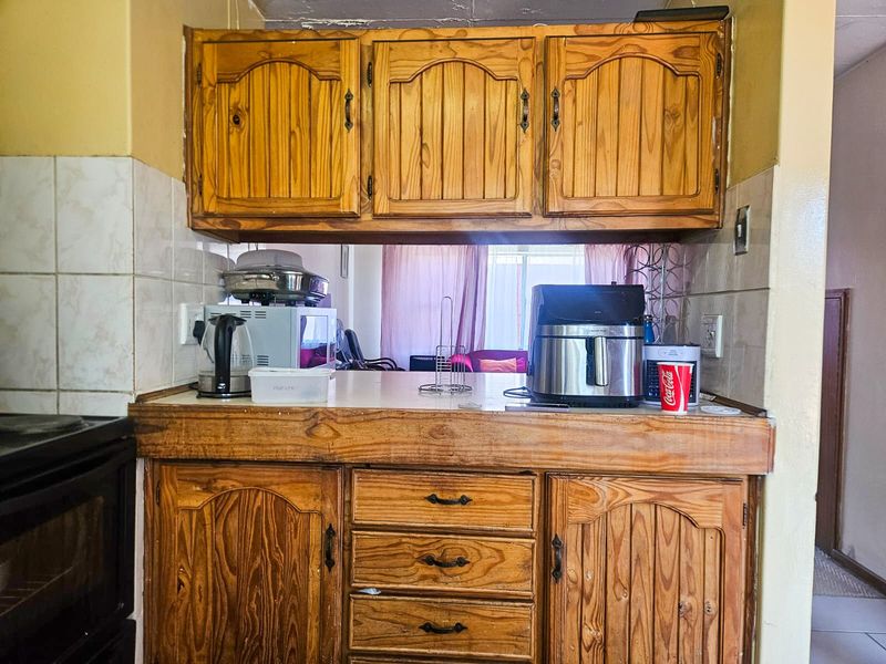 A dated kitchen featuring wooden cabinetry, laminate countertops, and a tiled backsplash, offering potential for a modern renovation.