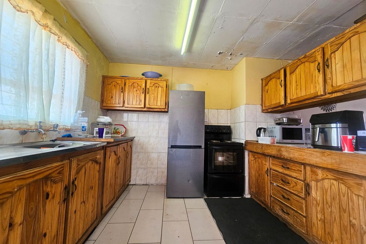 A dated kitchen featuring wooden cabinetry, tiled backsplash, and tiled flooring, requiring ceiling repairs and cosmetic updates to modernize the space.