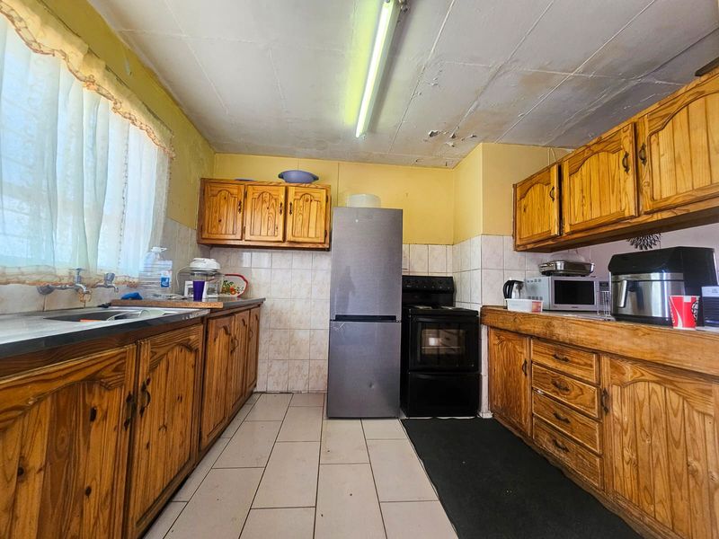 A dated kitchen featuring wooden cabinetry, tiled backsplash, and tiled flooring, requiring ceiling repairs and cosmetic updates to modernize the space.