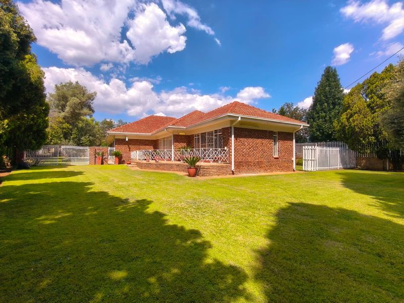A well-maintained face brick house featuring a tiled roof, a covered patio area, and expansive surrounding lawn with secure perimeter fencing.