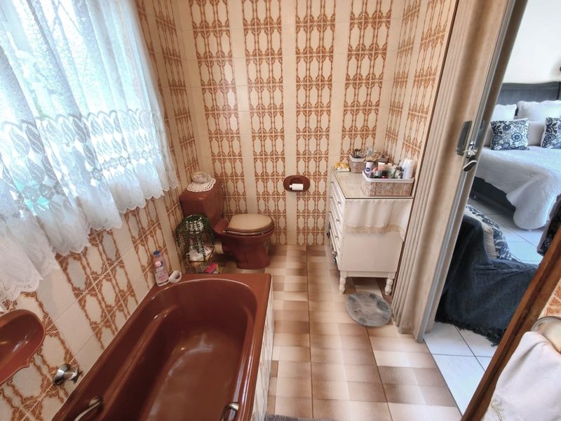 A dated bathroom featuring original brown sanitary ware, patterned wall tiles, and tiled flooring, offering significant potential for a modern renovation.