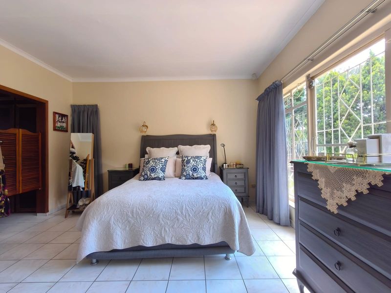 A well-lit bedroom featuring tiled flooring, built-in cupboard space, and large windows with security bars, offering a functional and comfortable living area.