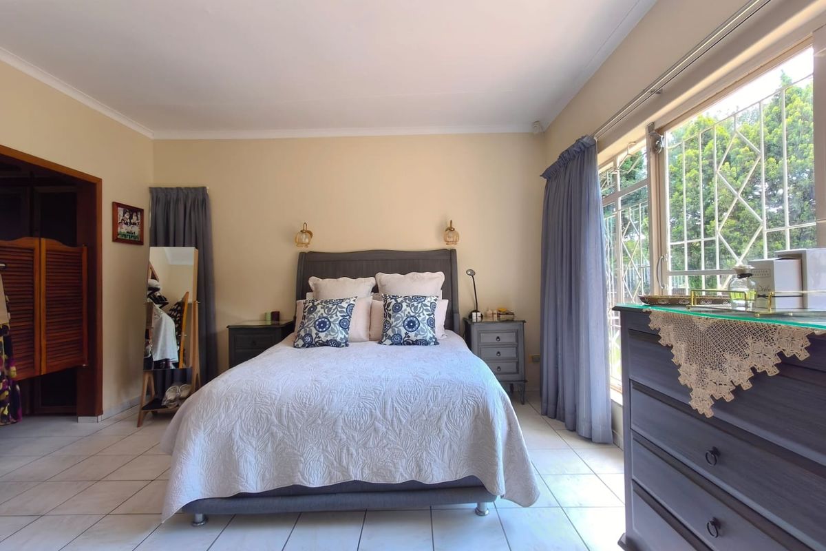 A well-lit bedroom featuring tiled flooring, built-in cupboard space, and large windows with security bars, offering a functional and comfortable living area.