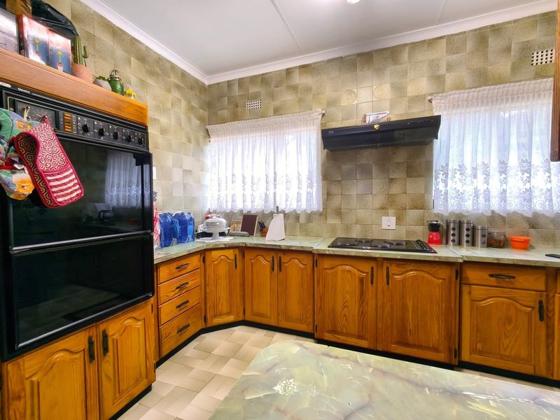A dated kitchen featuring traditional wooden cabinetry, built-in oven, hob, extractor fan, and patterned wall tiles, offering significant potential for a modern renovation.