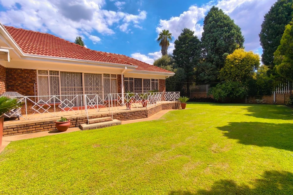 A well-maintained rear exterior view featuring a brick facade, tiled roof, and a spacious raised patio overlooking a large, manicured garden.