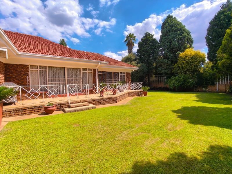 A well-maintained rear exterior view featuring a brick facade, tiled roof, and a spacious raised patio overlooking a large, manicured garden.