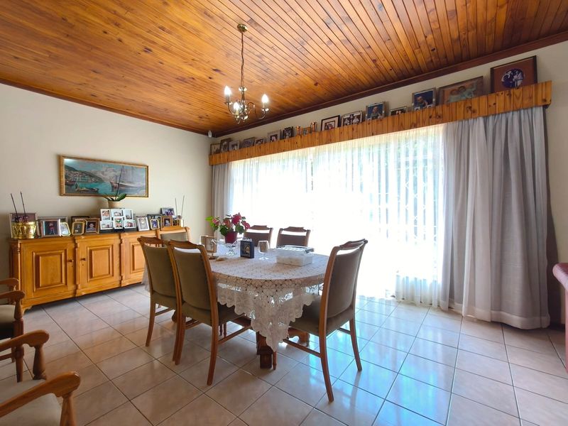A dining room featuring a warm timber tongue and groove ceiling, ceramic tiled flooring, and a large window with a built-in timber pelmet.