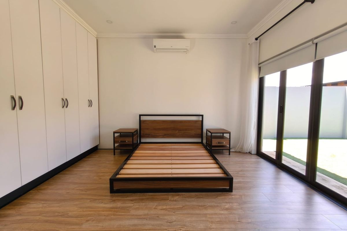 Spacious bedroom featuring built-in cupboards, laminate flooring, and large sliding glass doors providing direct access to the garden area.
