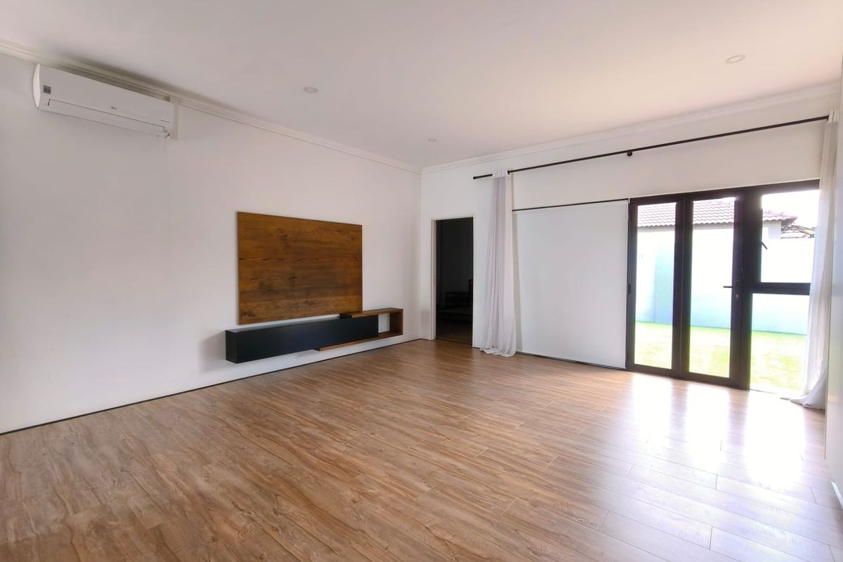 Spacious living area featuring wood-look laminate flooring, a wall-mounted media unit, split-system air conditioning, and direct access to the garden through sliding glass doors.