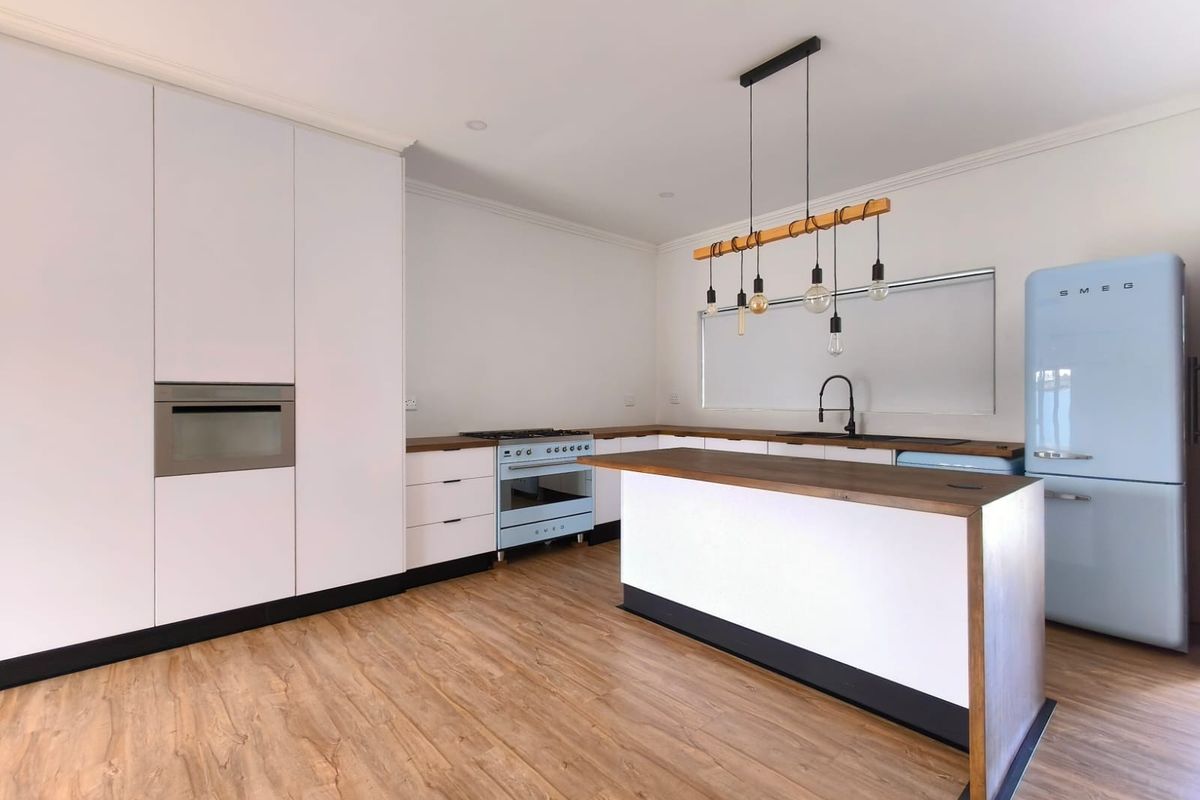 Modern kitchen featuring white cabinetry, timber countertops, a central island, built-in oven, gas cooktop, and stylish pendant lighting over the workspace.