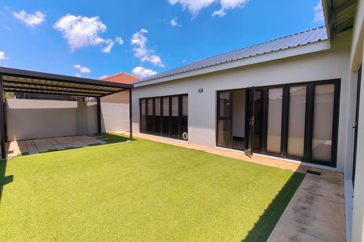 Rear exterior view featuring a low-maintenance artificial lawn, a covered patio area, and modern black-framed aluminium stacker doors leading into the home.