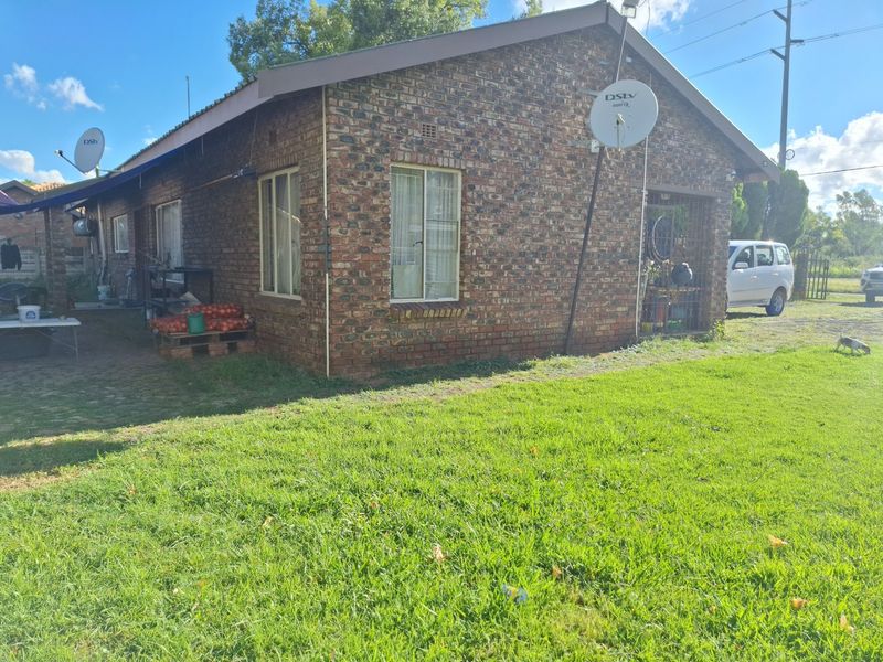 Rear view of a face brick house featuring a paved patio area, satellite dish, and surrounding garden space.