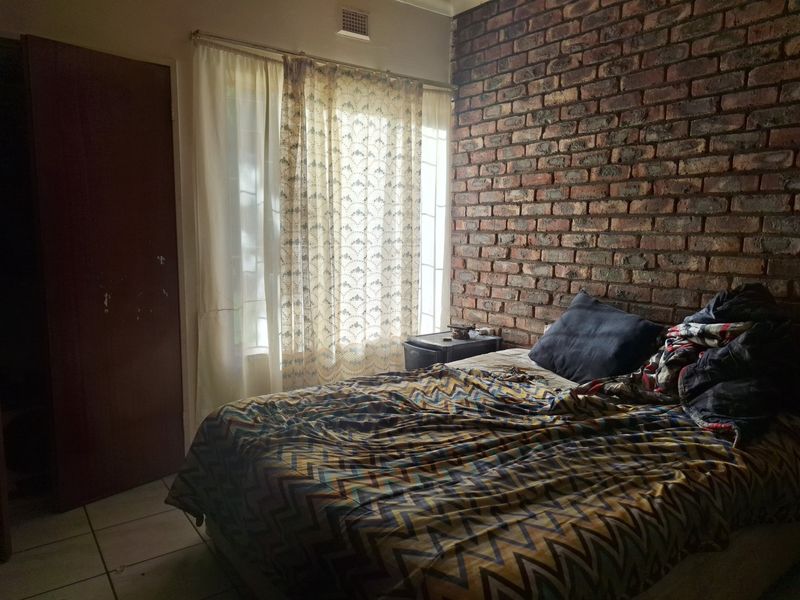 A bedroom featuring an exposed brick feature wall, tiled flooring, and natural light through a window with curtains.