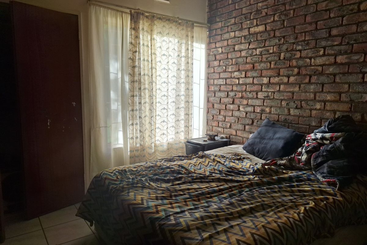 A bedroom featuring an exposed brick feature wall, tiled flooring, and natural light through a window with curtains.