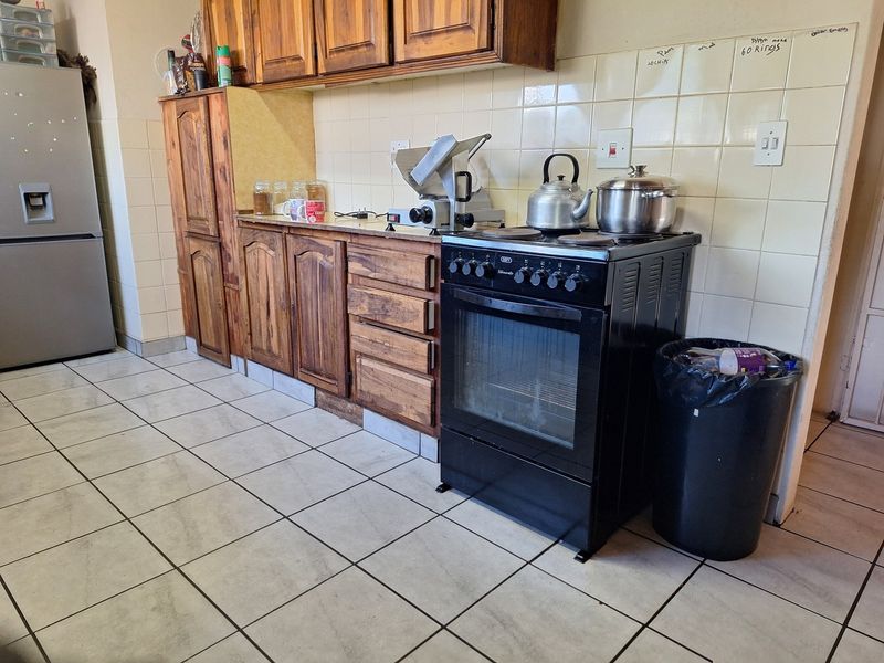 A functional kitchen featuring wooden cabinetry, tiled backsplash, and tiled flooring, equipped with a freestanding oven and hob.