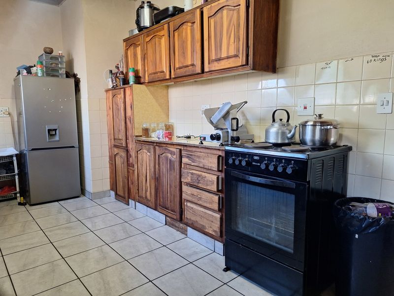 A functional kitchen featuring wooden cabinetry, tiled backsplash, and tiled flooring, equipped with a freestanding oven and hob.